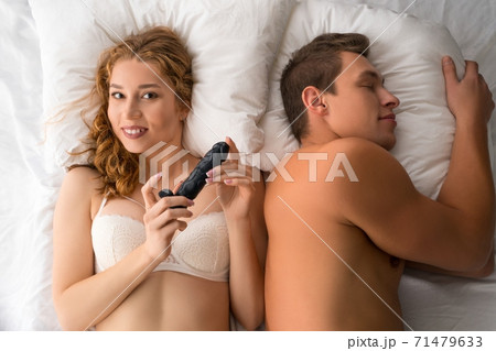 Playful woman in lingerie lying on bed with sleeping man 71479633