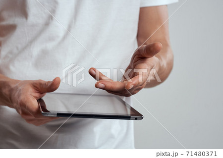 Tablet with a touch screen on a light background male hands white t-shirt cropped view Tablet with a touch screen on a light background male hands white t-shirt cropped view 71480371
