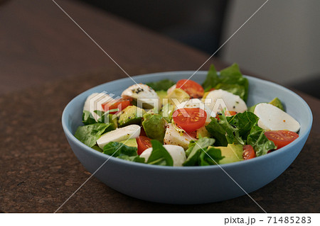 Salad with avocado, cherry tomatoes, romaine and mozzarella in blue bowl on walnut table with copy space Salad with avocado, cherry tomatoes, romaine and mozzarella in blue bowl on walnut table with copy space 71485283