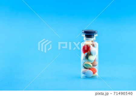 full transparent glass bottle with different colored pills closed by a stopper on a blue background, conceptual medical background with copy space. 71490540
