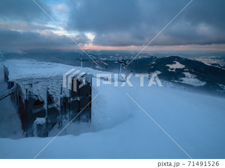 Alpine resortr ski lift with seats going over the sunset mountain skiing slopes in extremally windy weather Alpine resortr ski lift with seats going over the sunset mountain skiing slopes in extremally windy weather 71491526