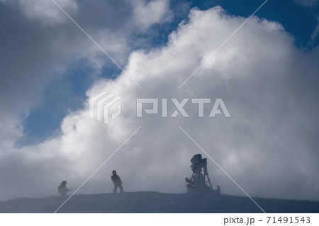 Snow covered winter mountain top in last evening sunlight before snowstorm. Windy frost on pointers and stop signs above dangerous precipice. People are unrecognizable. 71491543