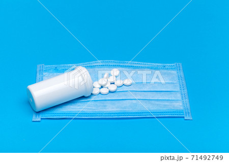 medical mask with a bottle of a medicinal product with a scattered pile of pills for the treatment of the respiratory tract of the lungs on a blue background with copy space. 71492749