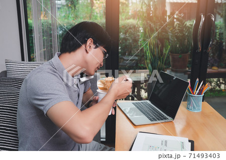 A man who works from home is busy talking on the phone with colleagues about work and eating instant noodles. While his eyes stared at the work content on the laptop as well. A man who works from home is busy talking on the phone with colleagues about work and eating instant noodles. While his eyes stared at the work content on the laptop as well. 71493403