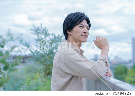 曇り空　ビルの屋上で電子タバコをすいながらほほえむ若い男性 71494328