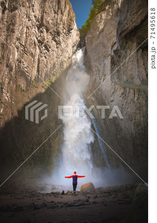 A full-length portrait of a young adult woman stands in front of a waterfall. The idea of a healthy lifestyle adventure and travel 71495618