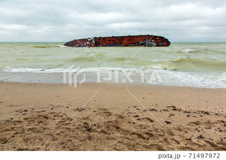 sandy beach in cloudy weather at sea with waves in the water on its side lies an inverted ship wrecked after a storm. sandy beach in cloudy weather at sea with waves in the water on its side lies an inverted ship wrecked after a storm. 71497972