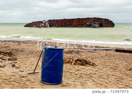 fighting the consequences of a tanker wreck on a sandy beach a protective barrier and a barrel for collecting oil waste. fighting the consequences of a tanker wreck on a sandy beach a protective barrier and a barrel for collecting oil waste. 71497973