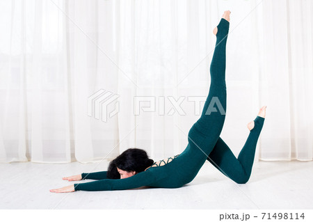 a woman in sportswear is doing a bending exercise and lifting one leg up on the floor side view of a bright gym with white curtains. a woman in sportswear is doing a bending exercise and lifting one leg up on the floor side view of a bright gym with white curtains. 71498114