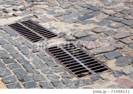the 2 iron grates of the drainage system hatch on the road paved with paving stones, closeup of a sewer grates. the 2 iron grates of the drainage system hatch on the road paved with paving stones, closeup of a sewer grates. 71498231