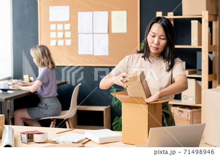 Young pretty worker of online shop office or store-room packing one of orders Young pretty worker of online shop office or store-room packing one of orders 71498946