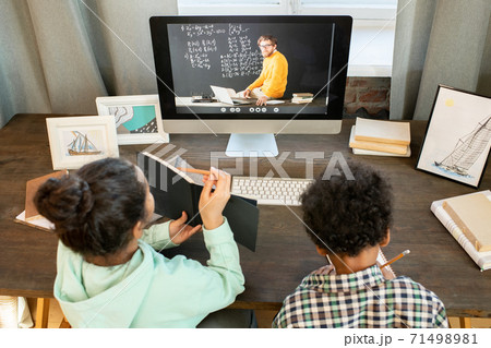 Diligent schoolgirl showing her notes in copybok to teacher on computer monitor 71498981