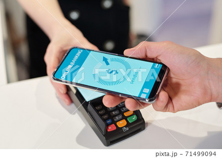 Hand of young man holding smartphone over terminal during contactless payment Hand of young man holding smartphone over terminal during contactless payment 71499094