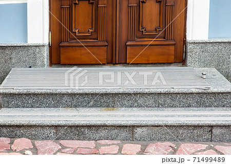 gray granite threshold with steps covered with non-slip rubber strips at the entrance wooden door of brown color at the facade of the building, front view close up. 71499489