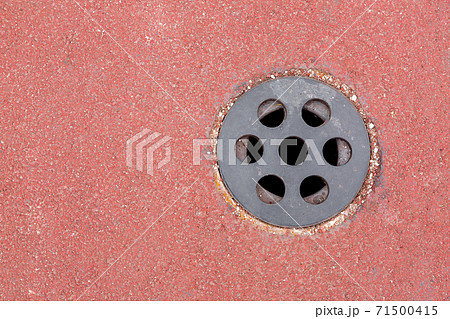 drainage hole with a round grid on a sports track made of red granular surface with copy space, top view close up. 71500415
