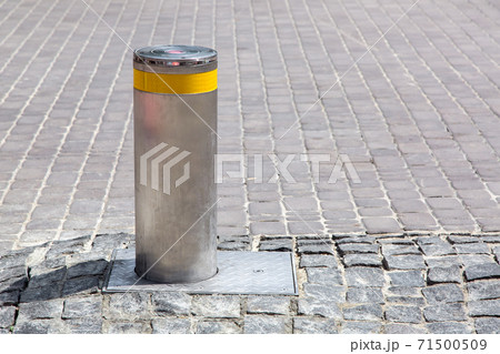 hydraulic gray electric bollard with a yellow reflective strip on the old stone tile road side view with copy space. hydraulic gray electric bollard with a yellow reflective strip on the old stone tile road side view with copy space. 71500509