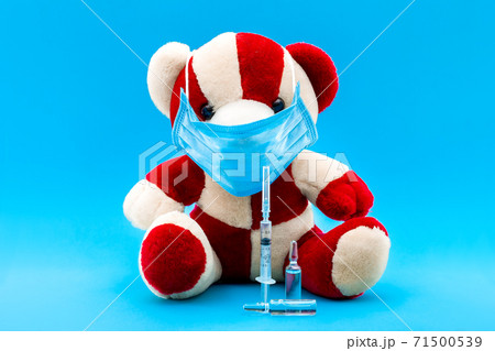 teddy bear in a medical mask with a syringe for vaccination and ampoules with a drug on a blue background with a copy space. 71500539