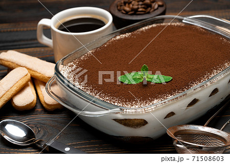 Traditional Italian Tiramisu dessert in glass baking dish, savoiardi cookies and cup of fresh hot espresso coffee on wooden background Traditional Italian Tiramisu dessert in glass baking dish, savoiardi cookies and cup of fresh hot espresso coffee on wooden background 71508603