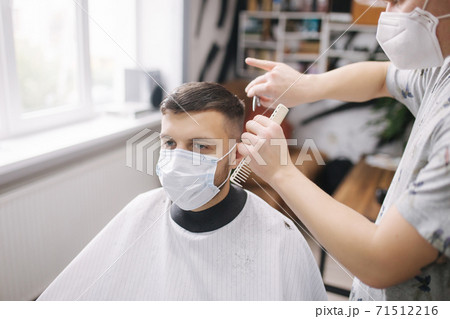 Man getting hair cut by scissor in barbershop. Barber use scissor and wearing mask during coronavirus pandemic. Professional barber work at home. Covid-19 quarantine Man getting hair cut by scissor in barbershop. Barber use scissor and wearing mask during coronavirus pandemic. Professional barber work at home. Covid-19 quarantine 71512216