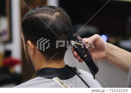 Back view of Men in beauty salon. Men's haircut in a barbershop. New haircut style 2021. Professional hairdresser uses a hair clipper for fringing hair Back view of Men in beauty salon. Men's haircut in a barbershop. New haircut style 2021. Professional hairdresser uses a hair clipper for fringing hair 71512224