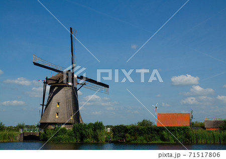 Kinderdijk, The Netherlands, August 2019. On a beautiful summer day a historic windmill, in perfect condition, in the Dutch countryside furrowed by canals lined with tall green grasses. Kinderdijk, The Netherlands, August 2019. On a beautiful summer day a historic windmill, in perfect condition, in the Dutch countryside furrowed by canals lined with tall green grasses. 71517806