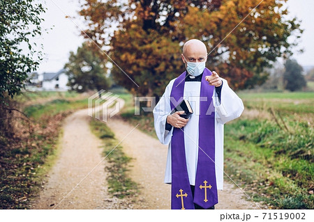 Catholic priest with a bible in a medical mask points with his finger 71519002