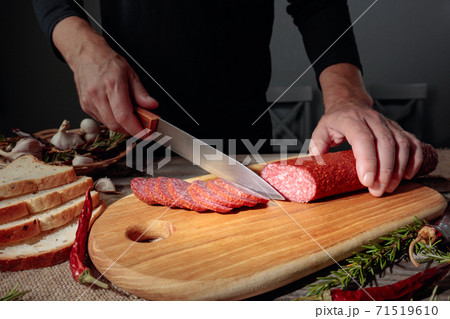 Man cuts a sausage for a sandwich. 71519610
