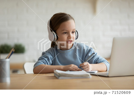 Focused little girl wearing headphones looking at laptop screen 71520609