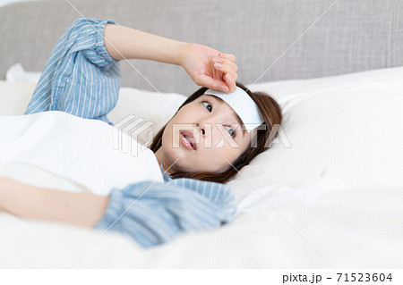 発熱してベッドの中でおでこを冷やす若い女性 発熱してベッドの中でおでこを冷やす若い女性 71523604