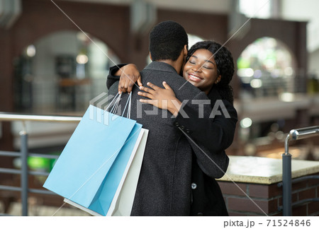 Happy young african american man and lady in coats hugs in city mall during seasonal sale and Black Friday Happy young african american man and lady in coats hugs in city mall during seasonal sale and Black Friday 71524846