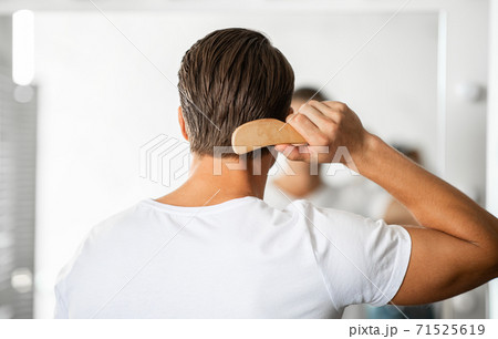 Young man looking in the mirror brushing hair Young man looking in the mirror brushing hair 71525619