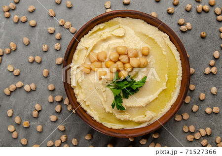 Flat lay view at hummus topped with green coriander leaves on stone table covered with chickpeas Flat lay view at hummus topped with green coriander leaves on stone table covered with chickpeas 71527366