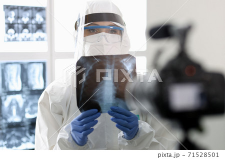 Doctor in protective suit shows an X-ray to camera. Doctor in protective suit shows an X-ray to camera. 71528501