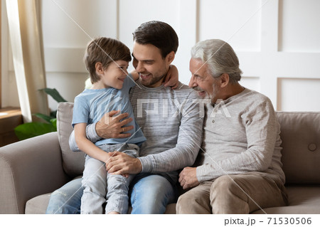 Happy three generations of men hugging, sitting on cozy couch Happy three generations of men hugging, sitting on cozy couch 71530506