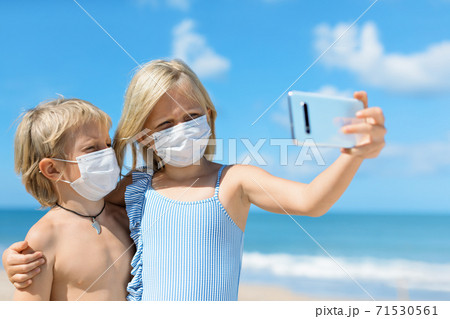Funny kids in face masks taking selfie photo on beach 71530561