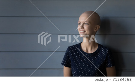 Smiling woman cancer patient standing near grey wall expressing courage Smiling woman cancer patient standing near grey wall expressing courage 71534568