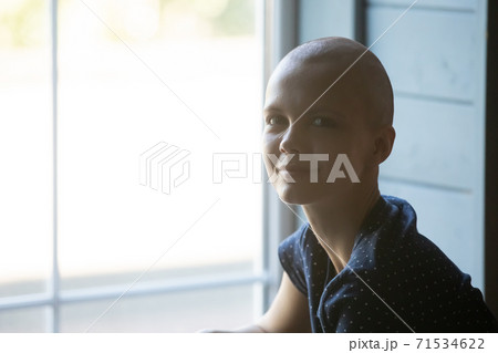 Calm smiling young woman receiving cancer treatment sitting by window Calm smiling young woman receiving cancer treatment sitting by window 71534622