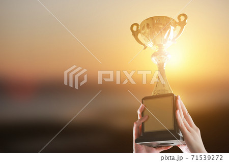 A man holding up a gold trophy cup on blur sunset background. copy space 71539272