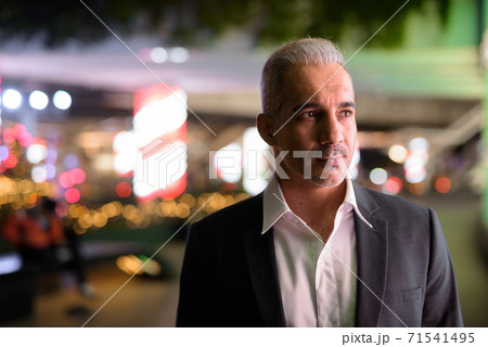 Portrait of handsome businessman wearing suit in city at night while thinking 71541495