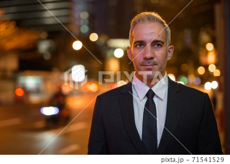 Portrait of handsome businessman wearing suit in city at night while thinking Portrait of handsome businessman wearing suit in city at night while thinking 71541529