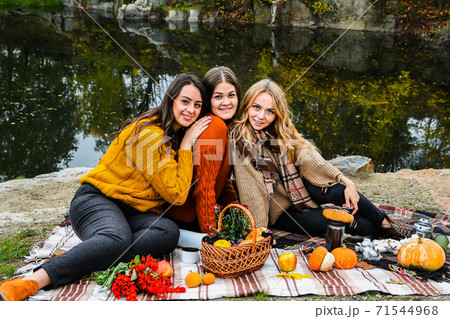 Three women best friends at autumn picnic in the park. Colorful plaid, thermos and pumpins. Friends having fun outdoors. 71544968