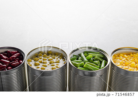 Canned kidney beans, green beans, peas and corn in opened tin cans on kitchen table. Non-perishable foods background 71546857