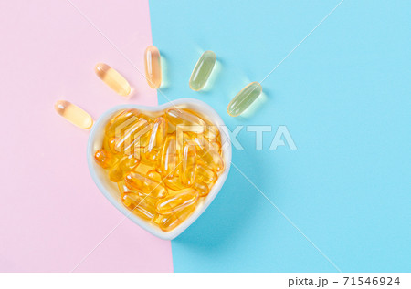 Fish oil capsules in white cup on blue background. 71546924