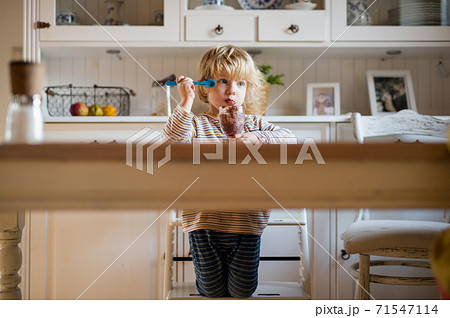 Small boy with dirty mouth indoors in kitchen at home, eating pudding. Small boy with dirty mouth indoors in kitchen at home, eating pudding. 71547114