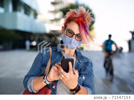 Senior woman with purple pink hair and smartphone outdoors in city, coronavirus concept. 71547153