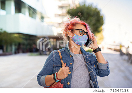 Senior woman with purple pink hair and smartphone outdoors in city, coronavirus concept. Senior woman with purple pink hair and smartphone outdoors in city, coronavirus concept. 71547158