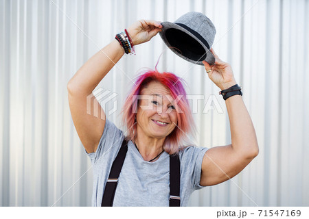 Senior woman with purple pink hair and hat standing against white background. Senior woman with purple pink hair and hat standing against white background. 71547169