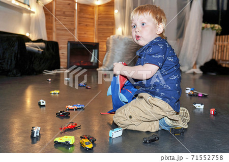 The child sits on the floor among the scattered toy cars 71552758