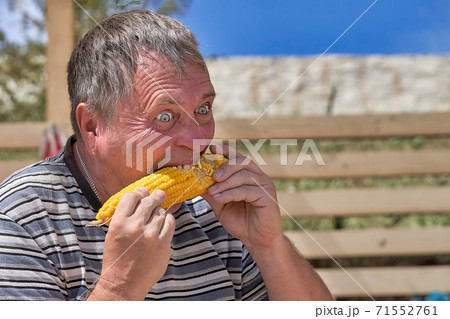 Freak with bulging eyes and open mouth holding an ear of corn 71552761