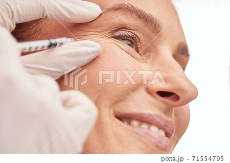 Beauty procedure. Close up of a beautiful mature woman receiving hyaluronic acid injection by beautician Beauty procedure. Close up of a beautiful mature woman receiving hyaluronic acid injection by beautician 71554795
